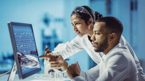 Two lab technicians discussing results displayed on a computer screen